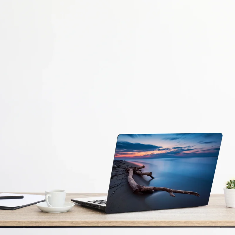 Naklejka na laptopa dryfujące drewno o zmierzchu na spokojnej plaży